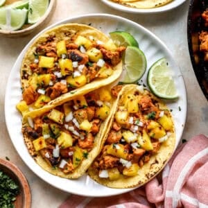 Chicken Al Pastor served in tacos with toppings and lime wedges.