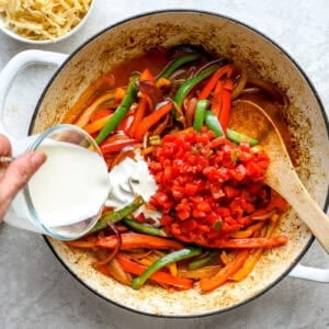Tomatoes and cream being added to sauteed vegetables.