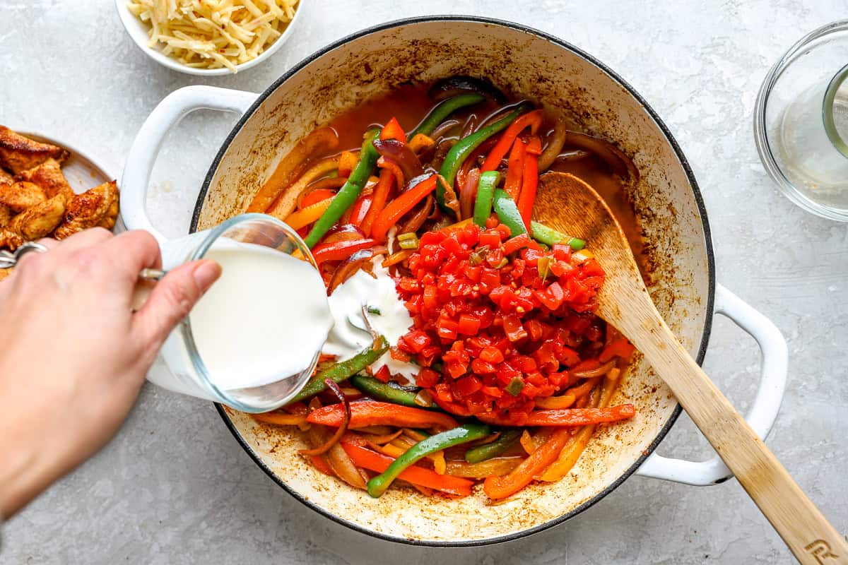 Pouring cream into a pot of fajita peppers and diced tomatoes.