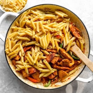 Pasta and chicken being stirred into the skillet.