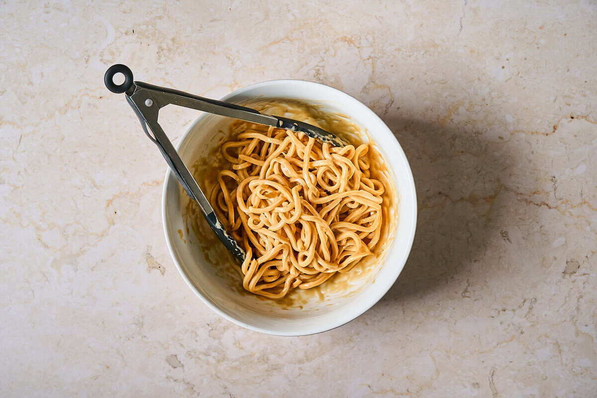 Cold udon noodles being tossed in tahini dressing.