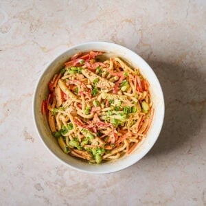 Cold chicken noodle salad in a bowl with garnish.
