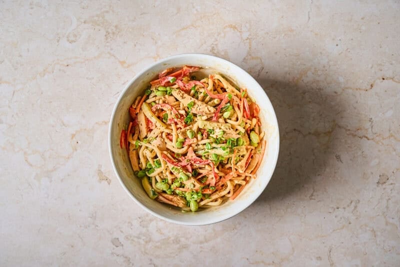 Cold chicken noodle salad in a bowl with garnish.