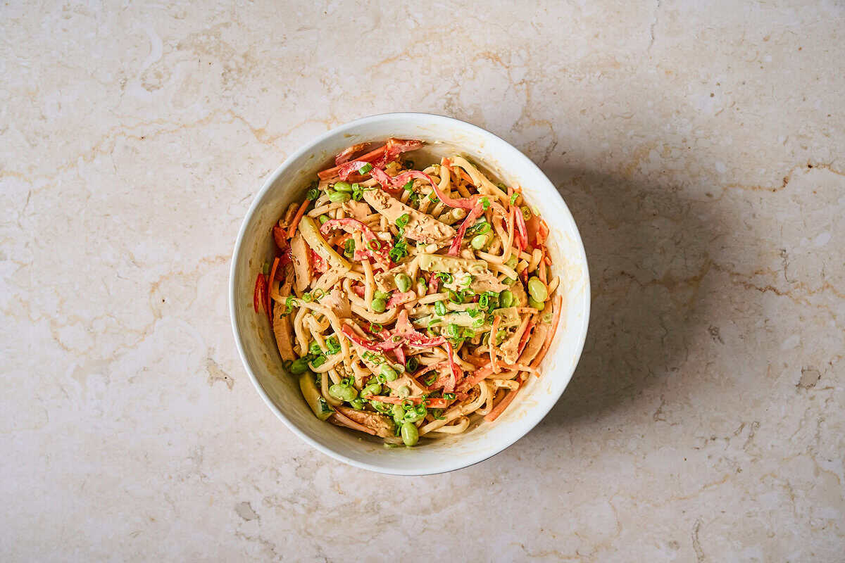 Cold chicken noodle salad in a bowl with garnish.