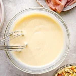 Soup, milk, butter and mustard being whisked together in a bowl.