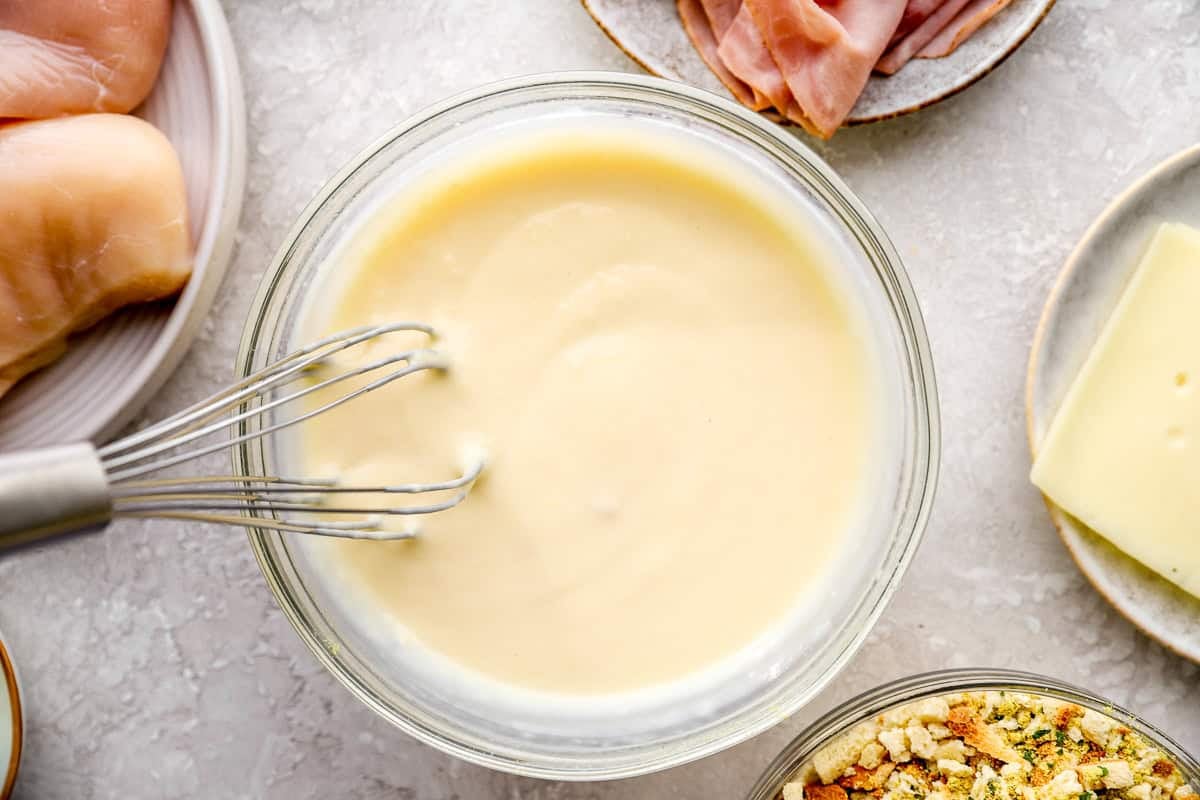 Soup, milk, butter and mustard being whisked together in a bowl.