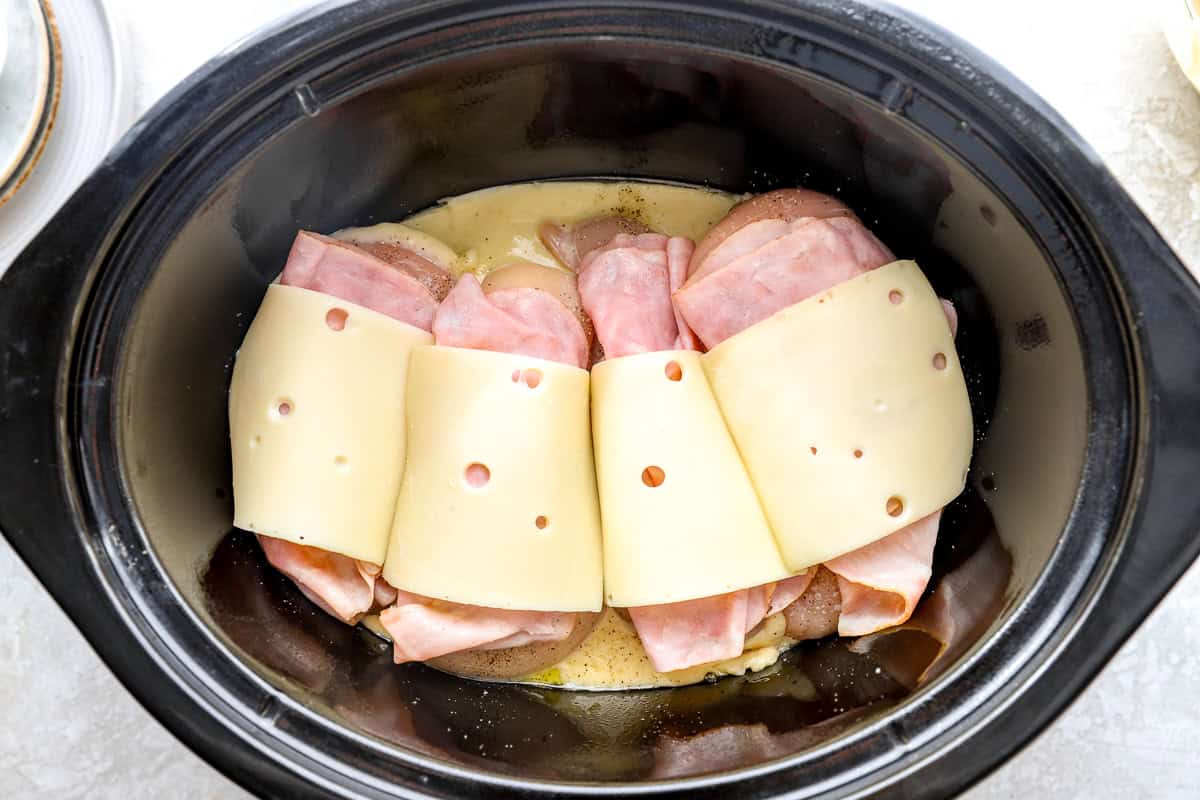 Cheese and ham on top of chicken breasts in a slow cooker.