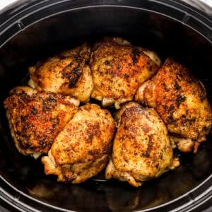Chicken thighs and broth in a slow cooker.