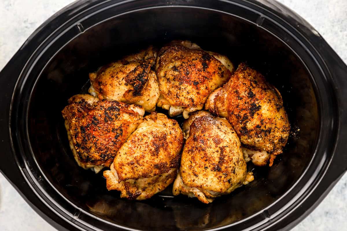 Chicken thighs and broth in a slow cooker.