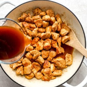 Diet cola sauce being poured over browned chicken in a skillet.