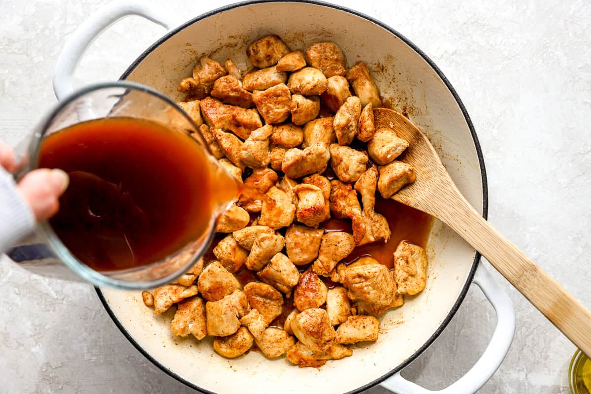 Diet cola sauce being poured over browned chicken in a skillet.
