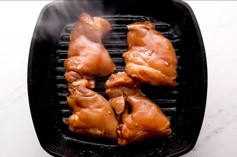 Marinated chicken thighs on a grill.