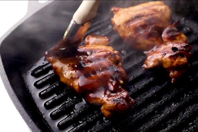 Basting chicken thighs with huli huli sauce as they cook on the grill.