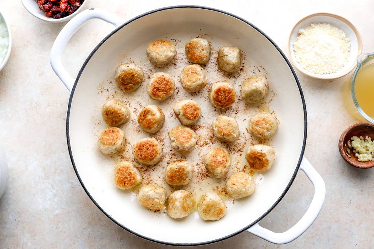 Browned chicken meatballs in a skillet.