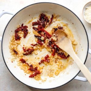 Onions and sundried tomatoes cooking in a skillet.