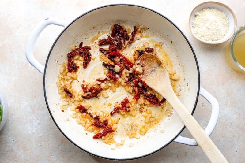 Onions and sundried tomatoes cooking in a skillet.
