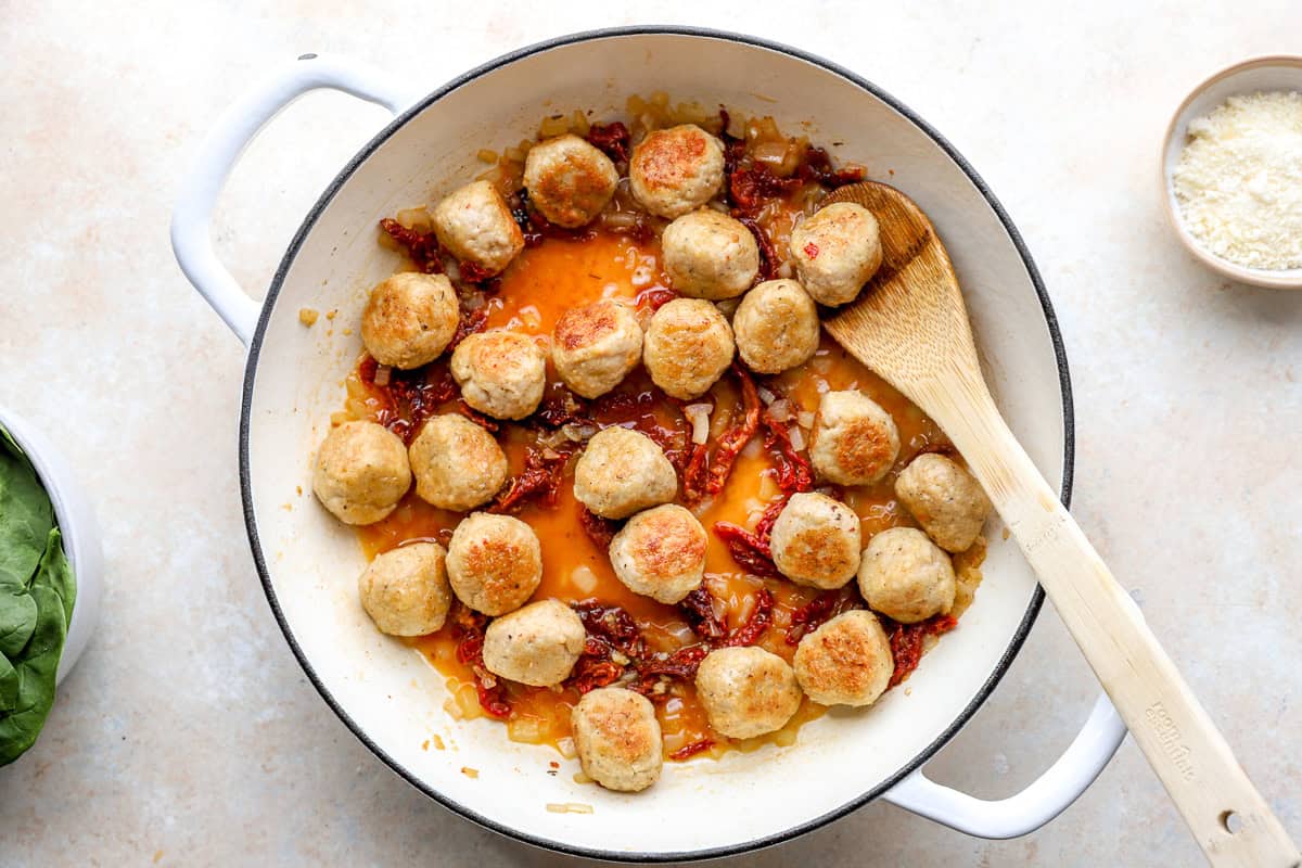 Chicken meatballs cooking with sun-dried tomatoes and onion.