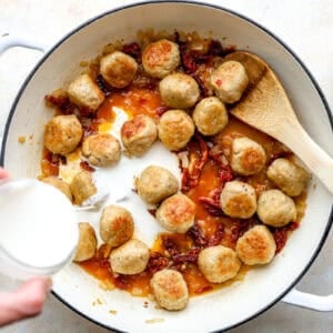 Cream being poured into a skillet with meatballs.
