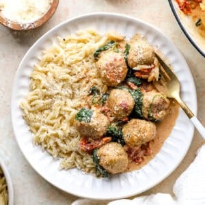 Chicken meatballs in a Tuscan sauce served with orzo on a white plate.