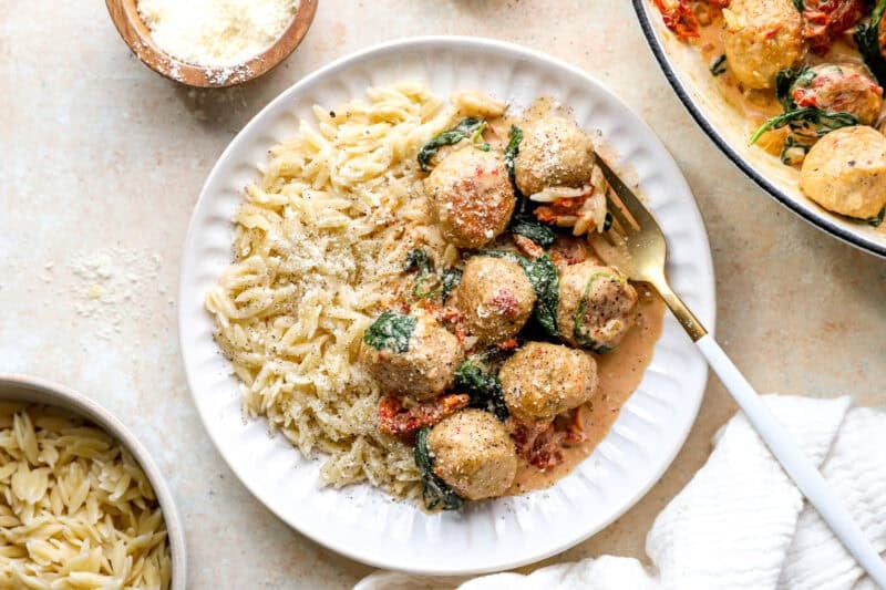 Chicken meatballs in a Tuscan sauce served with orzo on a white plate.