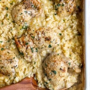 Wooden spoon digging into chicken thighs and rice casserole.