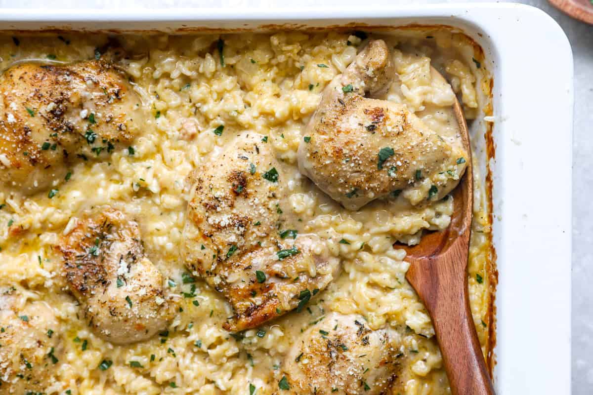 Wooden spoon digging into chicken thighs and rice casserole.