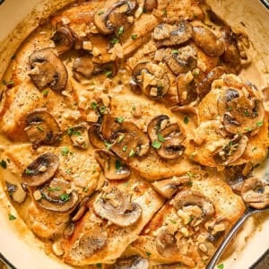 A metal serving spoon inside a skillet of creamy chicken diane.