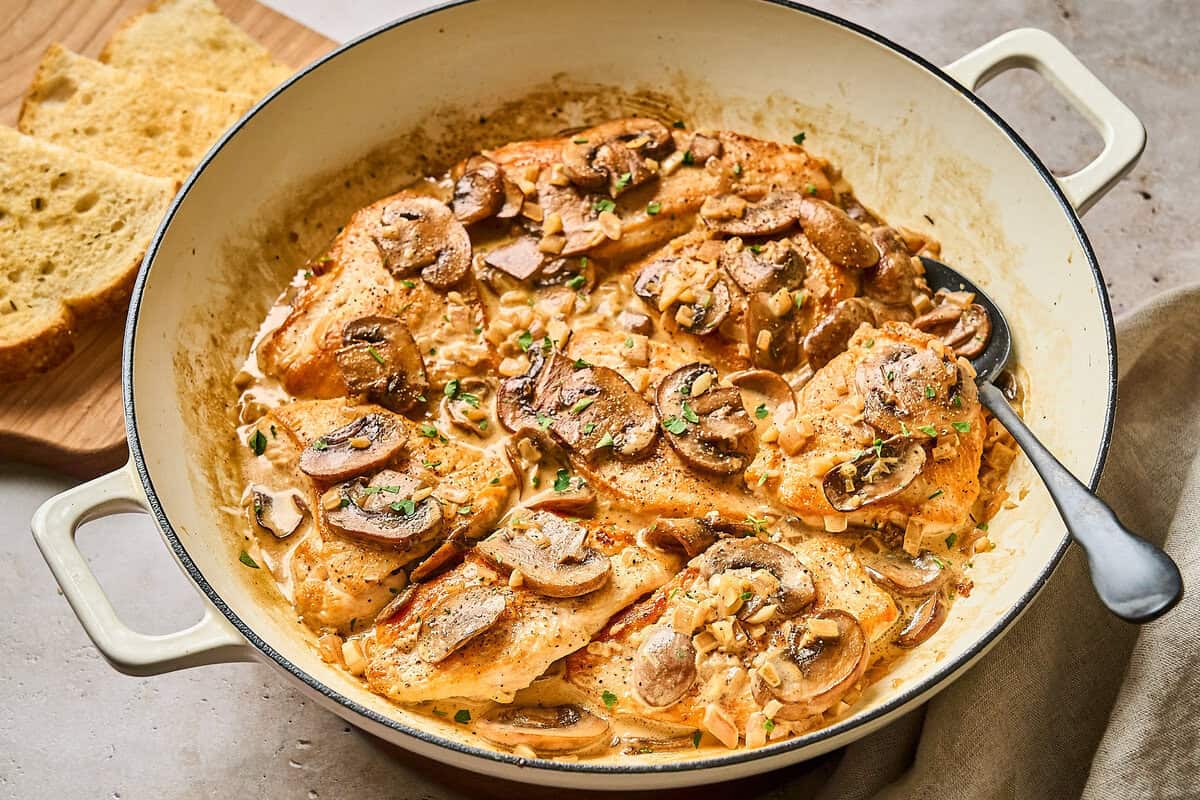 Creamy chicken Diane in brandy sauce with mushrooms; in a skillet with a metal spoon ready to serve.