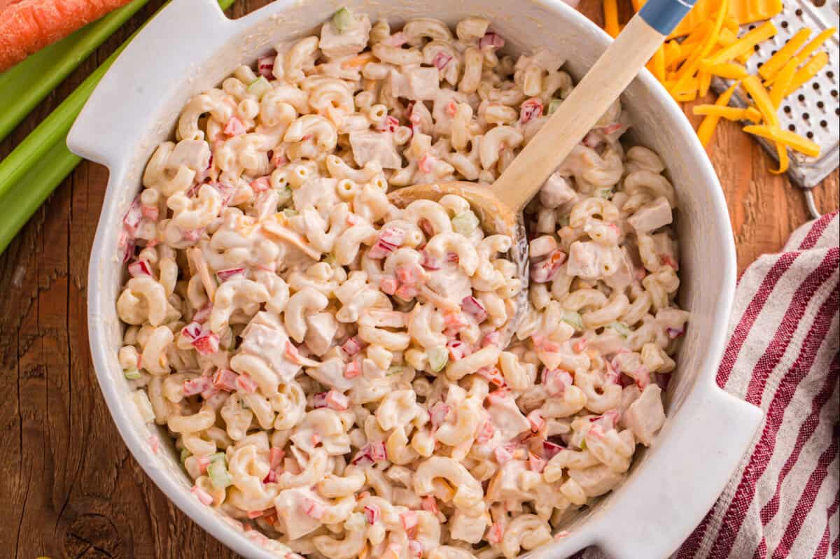 Chicken macaroni pasta salad in a white serving bowl with a wooden spoon.