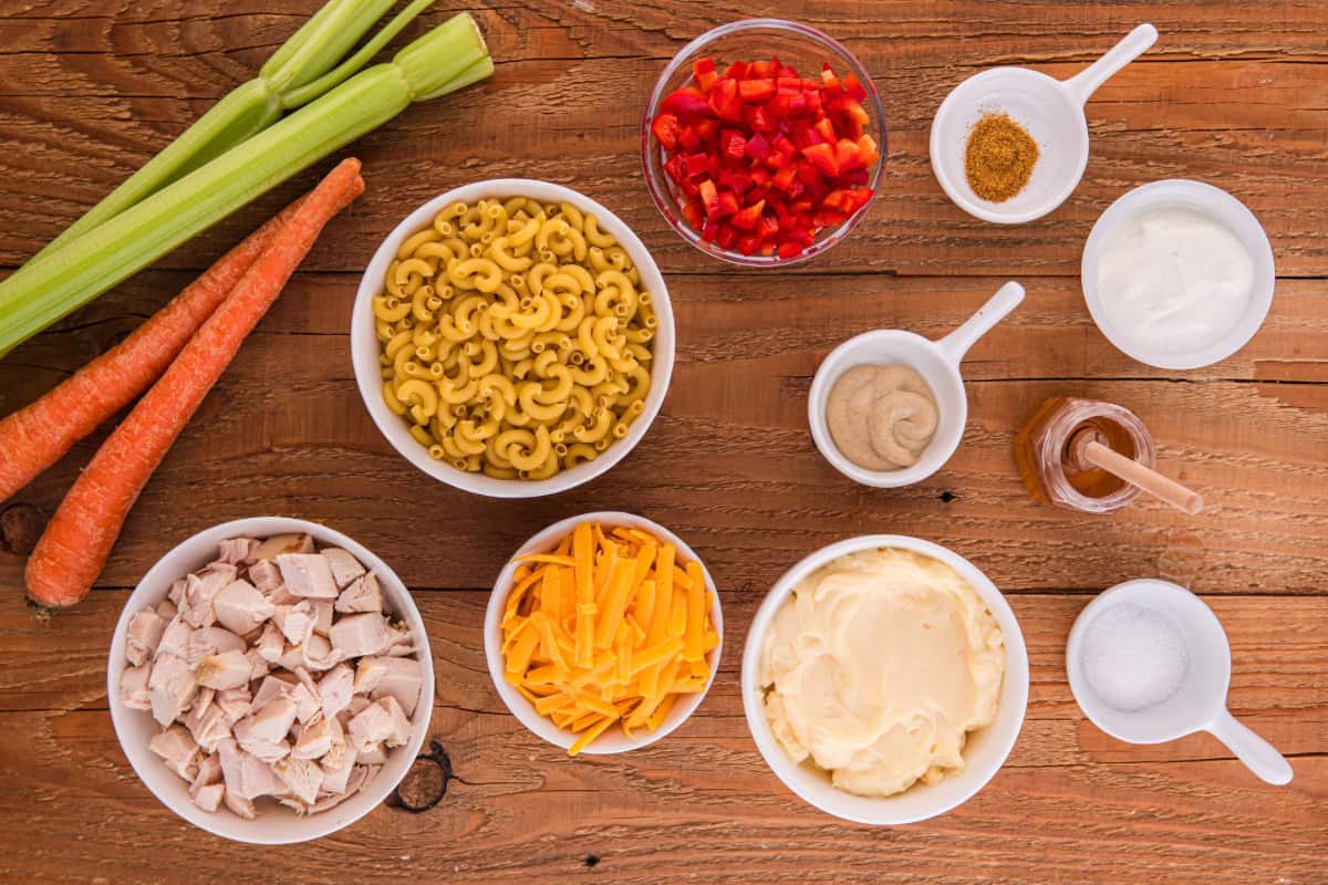 Chicken macaroni salad ingredients include elbow macaroni, mayonnaise, sour cream, dijon mustard, honey, salt, paprika, diced chicken, shredded cheddar cheese, diced celery, red bell pepper, and chopped carrots.