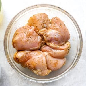 Raw seasoned chicken thighs in a glass bowl.