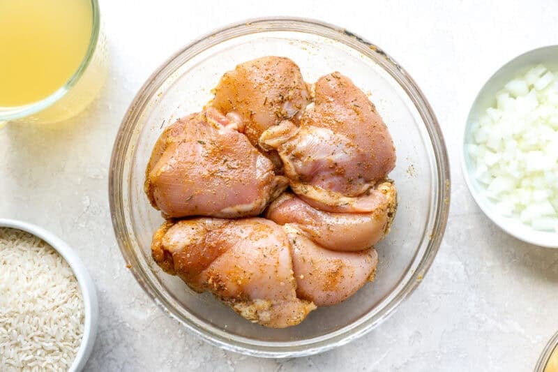 Raw seasoned chicken thighs in a glass bowl.
