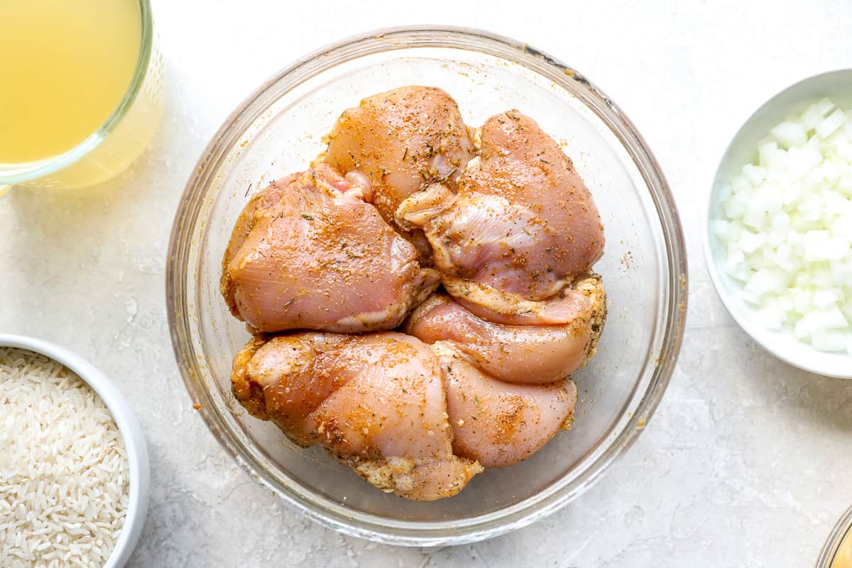 Raw seasoned chicken thighs in a glass bowl.
