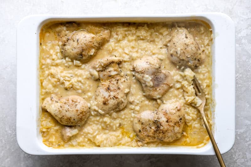 Chicken thighs in a creamy rice mixture, in a baking dish.