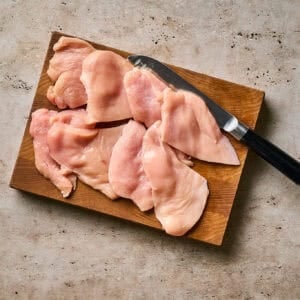 Raw chicken cutlets on a wooden cutting board with a knife.