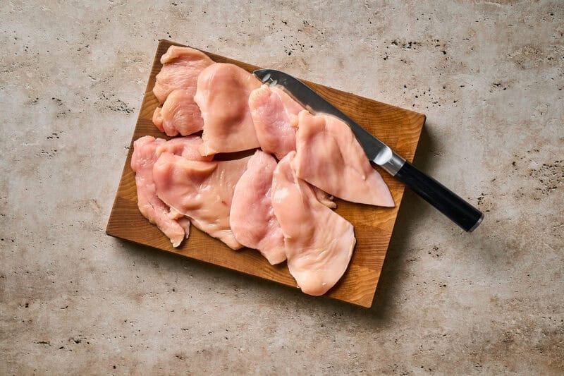 Raw chicken cutlets on a wooden cutting board with a knife.