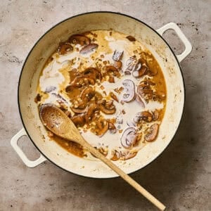 Stirring heavy cream into a skillet of creamy chicken diane sauce with a wooden spoon.