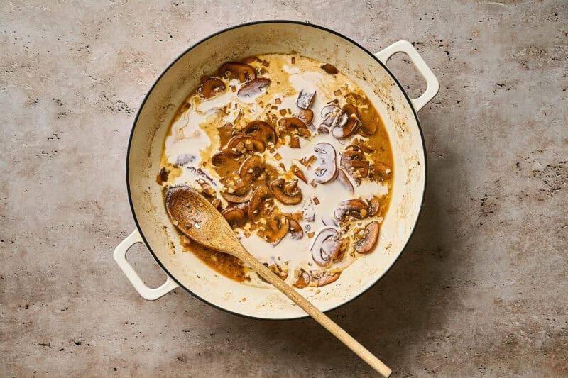 Stirring heavy cream into a skillet of creamy chicken diane sauce with a wooden spoon.