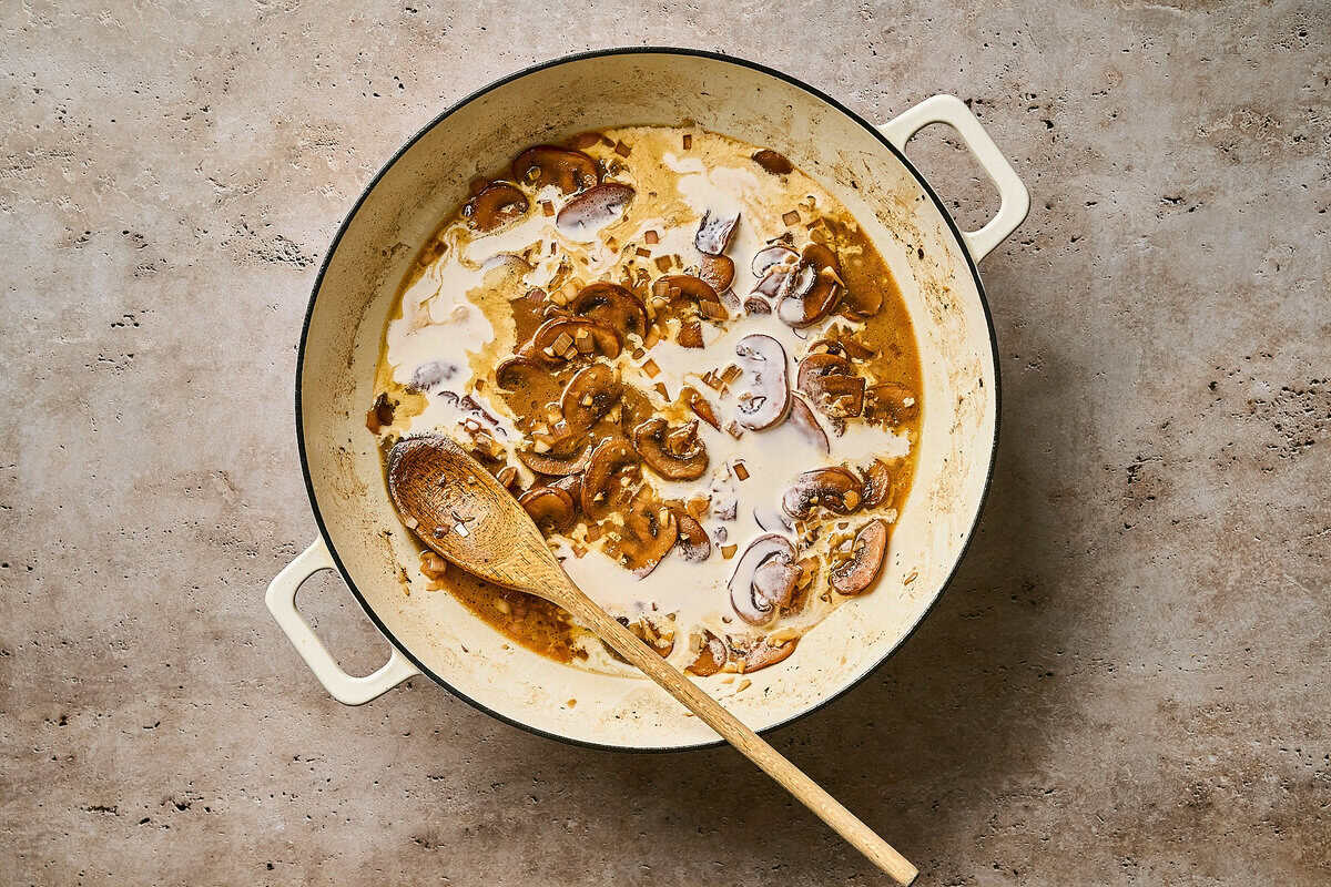 Stirring heavy cream into a skillet of creamy chicken diane sauce with a wooden spoon.