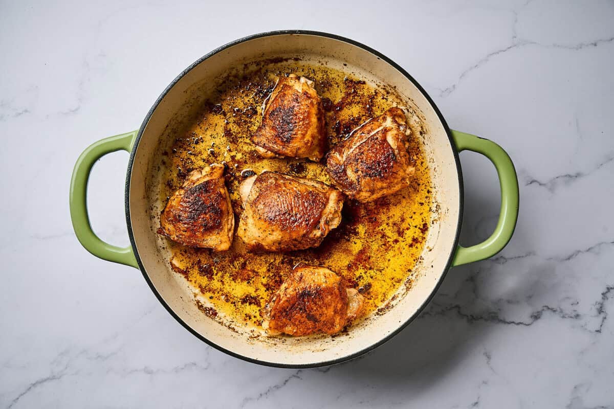 Cooked chicken in a skillet over a white marble surface.