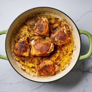 Cooked chicken in a skillet over a white marble surface.