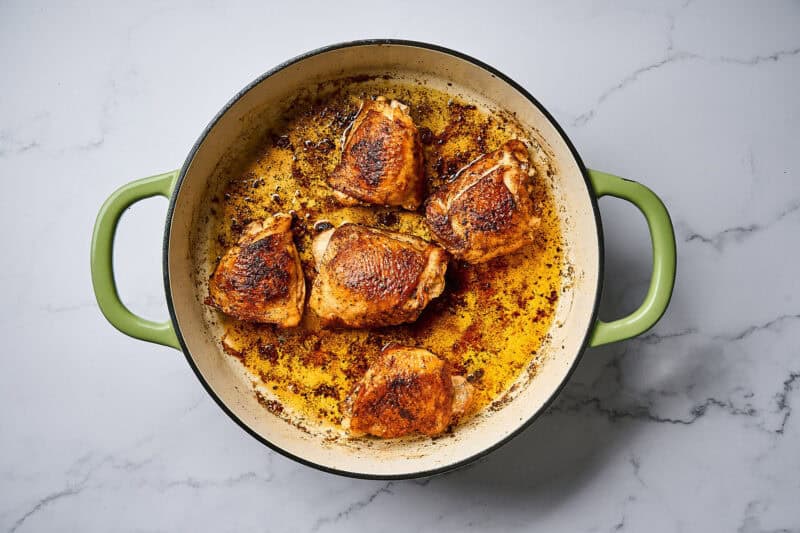 Cooked chicken in a skillet over a white marble surface.
