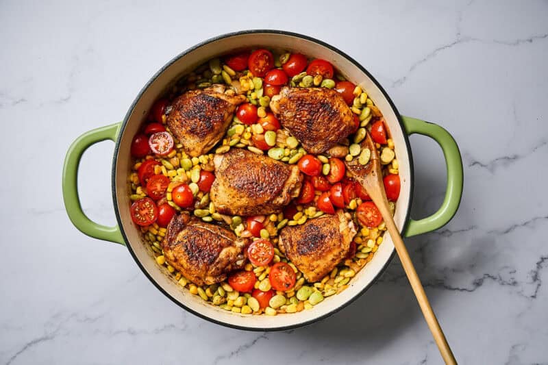 Cooked chicken thighs in a skillet with succotash.