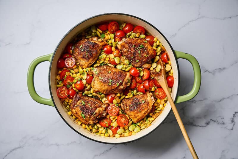 Chicken thighs and corn succotash in a skillet, garnished with cilantro.