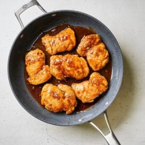 Chicken thighs in the sauce in a skillet.