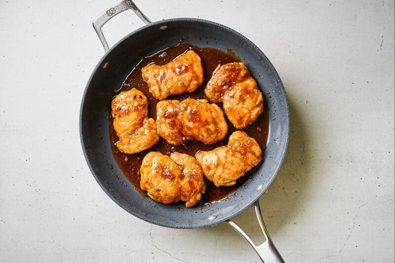 Chicken thighs in the sauce in a skillet.