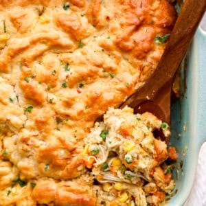 Wooden spoon digging into chicken cobbler casserole, to reveal the shredded chicken and veggie filling.