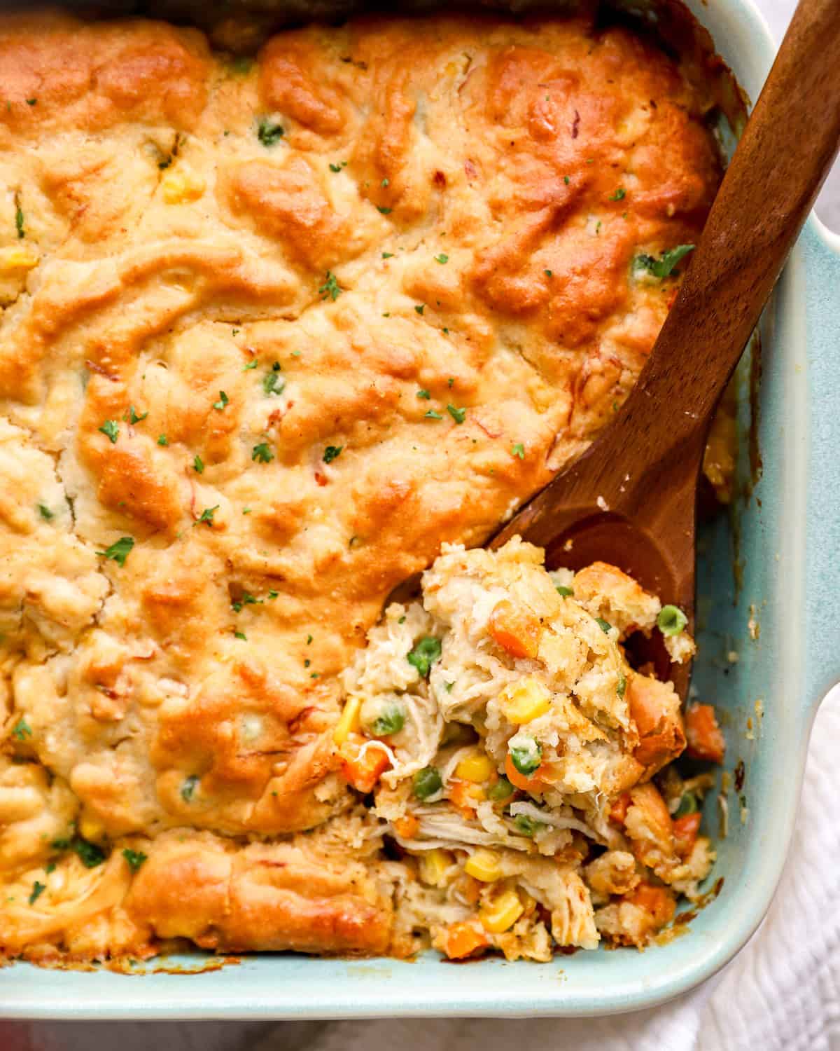 Wooden spoon digging into chicken cobbler casserole, to reveal the shredded chicken and veggie filling.