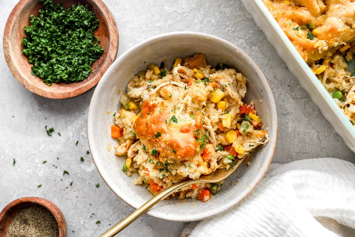A white bowl of chicken cobbler surrounded by ingredients.