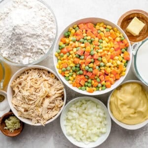 Ingredients for chicken cobbler, featuring butter, onion, salt, pepper, garlic, frozen mixed vegetables, cream of chicken soup, chicken broth, all-purpose chicken seasoning, shredded chicken, biscuit mix, and milk.